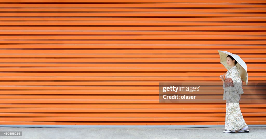 Kimono woman walking in front of monochrome wall