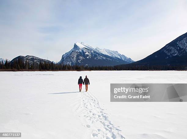 young couple walking on frozen lake - canadian rockies stock pictures, royalty-free photos & images