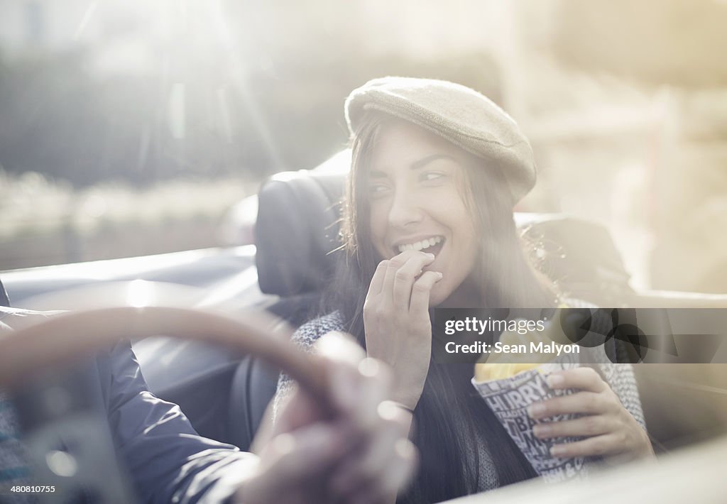 Young couple in convertible, woman eating chips