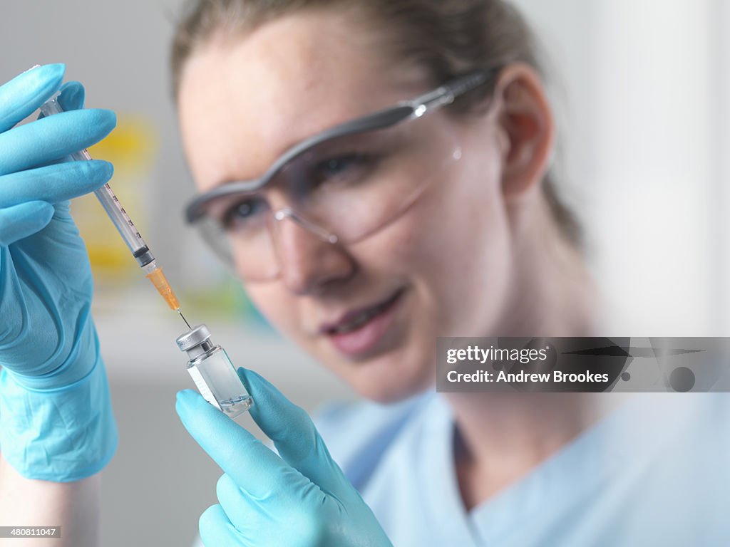 Healthworker holding up a syringe and vial, filling syringe in preparation injection