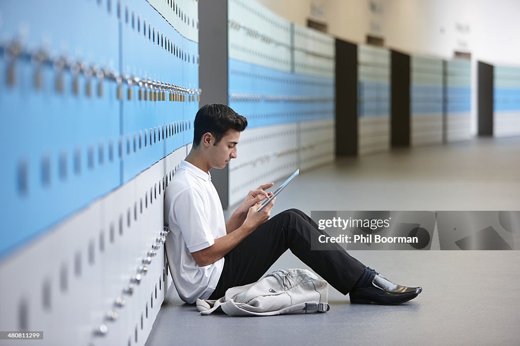 Portrait of teenage schoolboy sitting on floor next to lockers