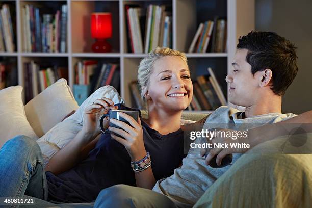 young couple sitting on sofa with hot drinks - night in stock pictures, royalty-free photos & images