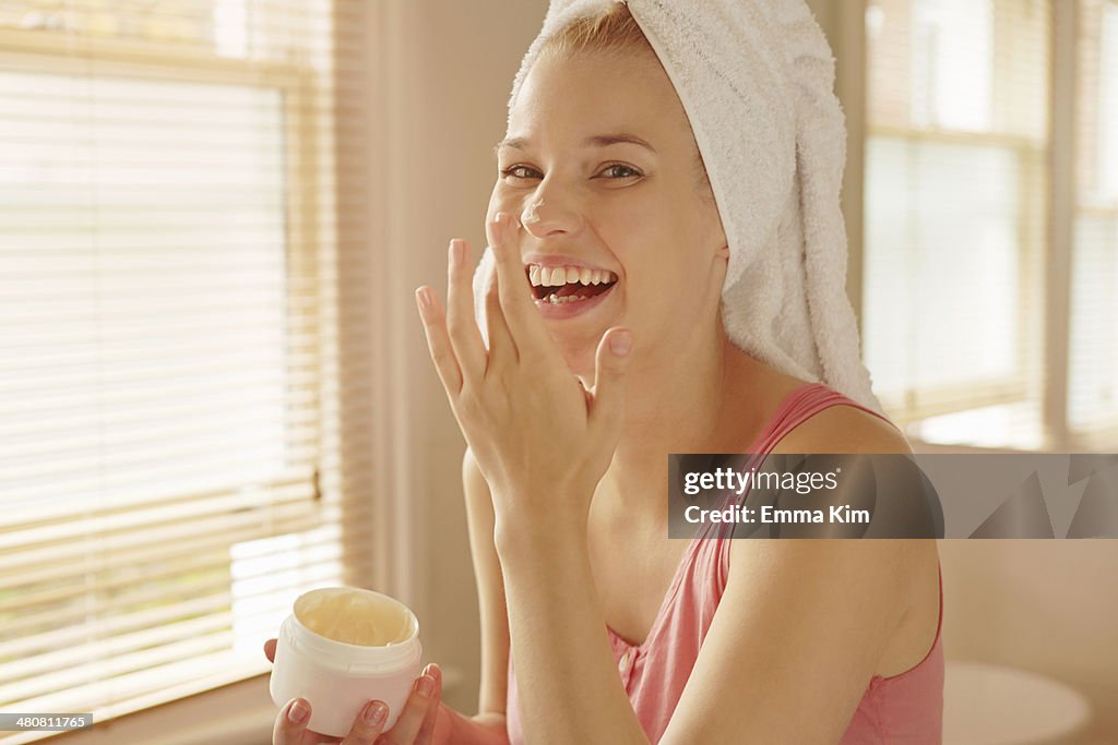 Young woman in bathroom putting on face cream