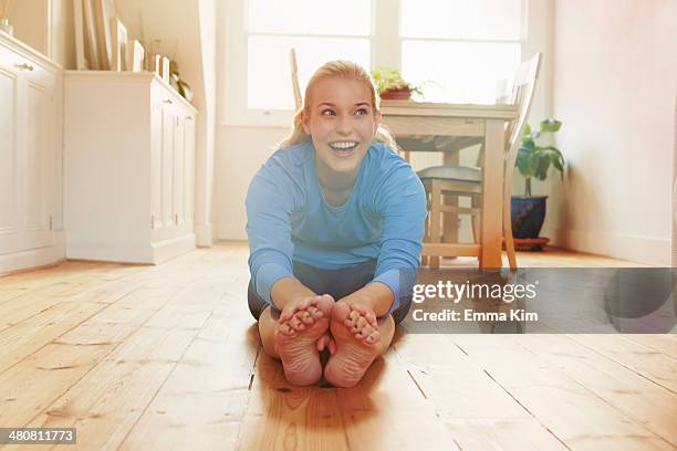 young woman sitting on floor leaning forwards touching toes - zehenspitzen berühren stock-fotos und bilder