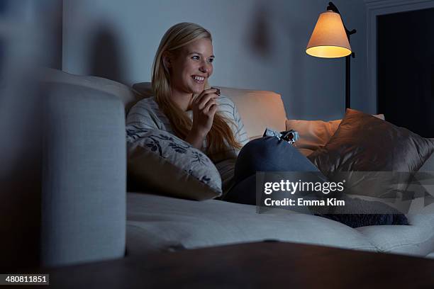 young woman sitting on sofa, watching tv, eating chocolate - woman enjoying night stock-fotos und bilder