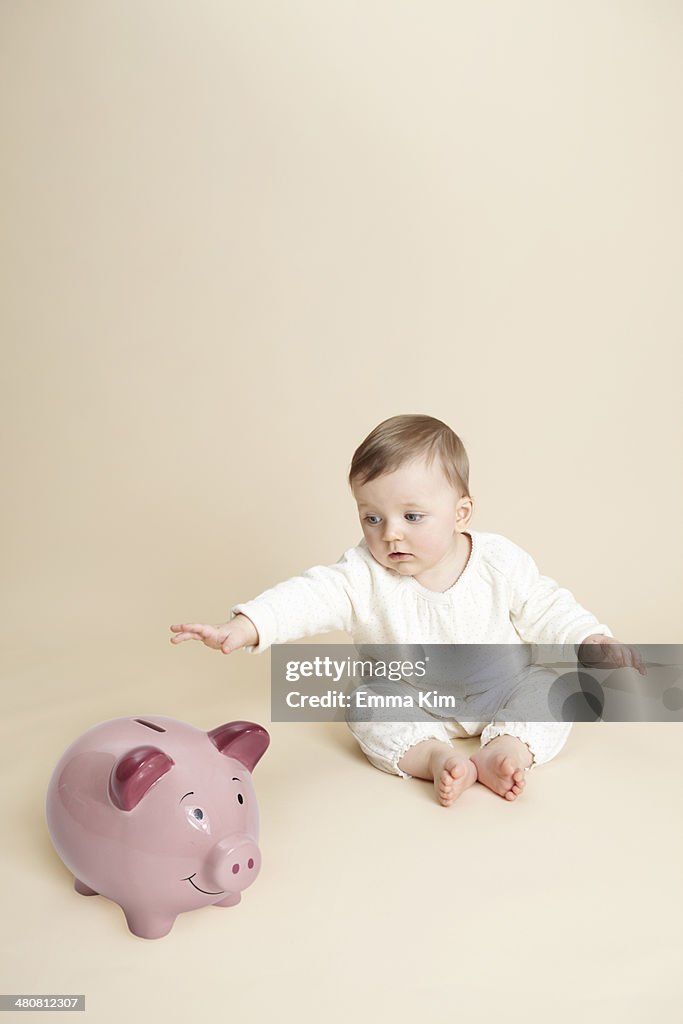 Studio portrait of baby girl reaching for piggy bank