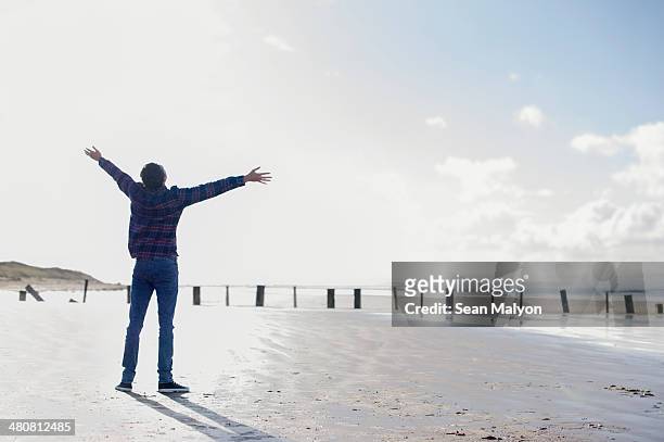 young man standing on beach with arms out, brean sands, somerset, england - sean malyon stock pictures, royalty-free photos & images