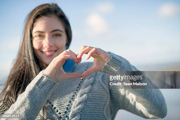 young woman making heart shape with hands - sean malyon stock-fotos und bilder