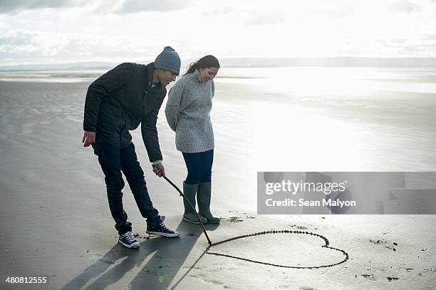 young couple drawing heart in sand, brean sands, somerset, england - sean malyon stock pictures, royalty-free photos & images