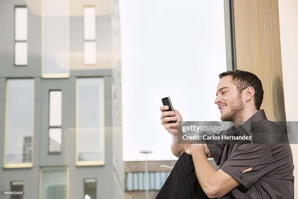 Businessman sitting on windowsill using smartphone