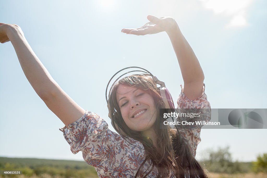 Portrait of mid adult woman dancing in field wearing headphones with arms raised