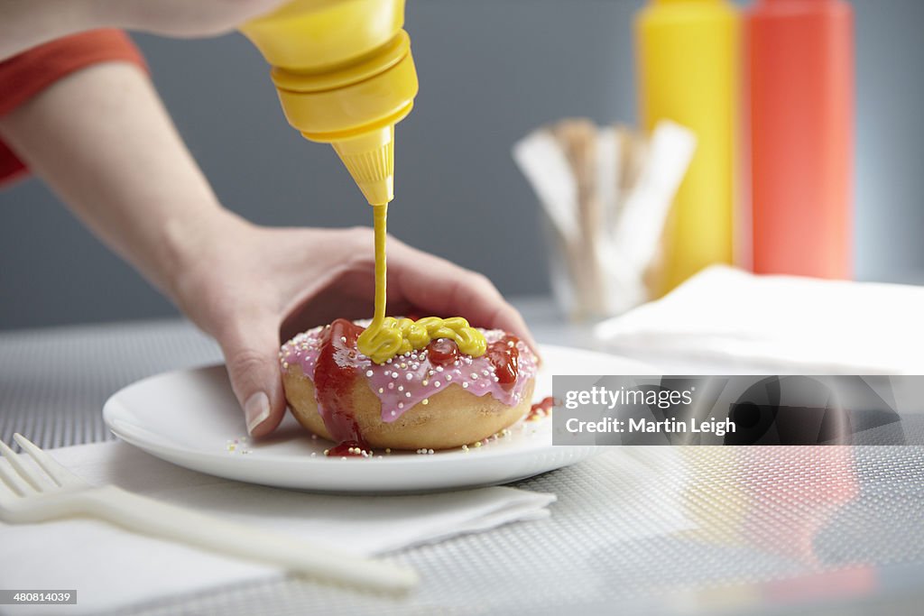 Woman squirting donut with ketchup and mustard