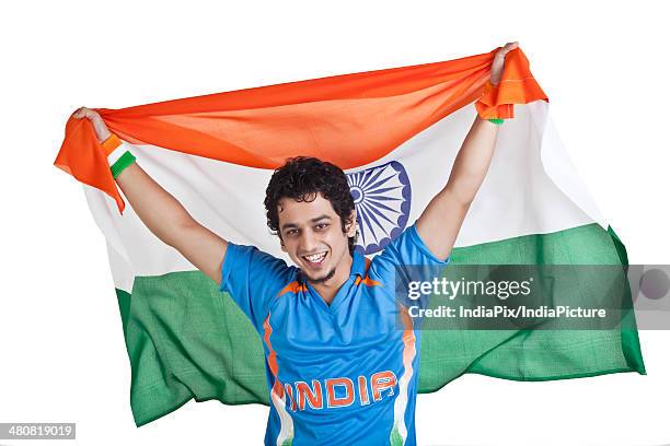 portrait of young man in indian cricket team jersey holding national flag over white background - cricket jersey stock pictures, royalty-free photos & images