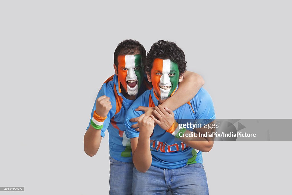 Excited male cricket supporters with face painted in tricolor cheering over gray background