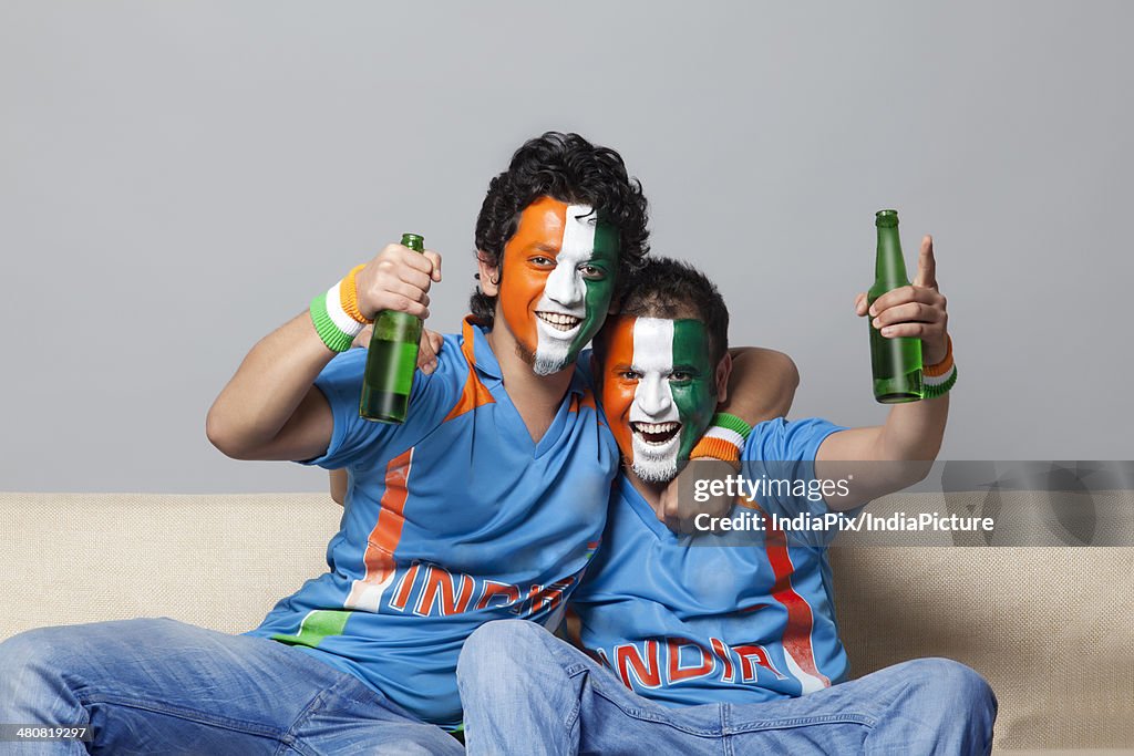 Portrait of happy male friends with face painted in tricolor enjoying beer together at home