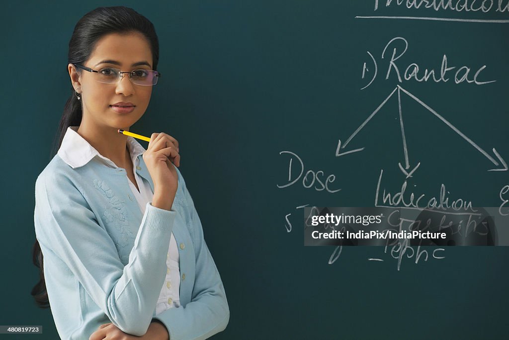 Portrait of confident young teacher against blackboard
