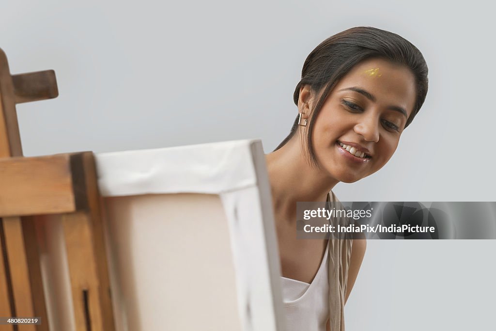 Young Indian woman painting on canvas over gray background