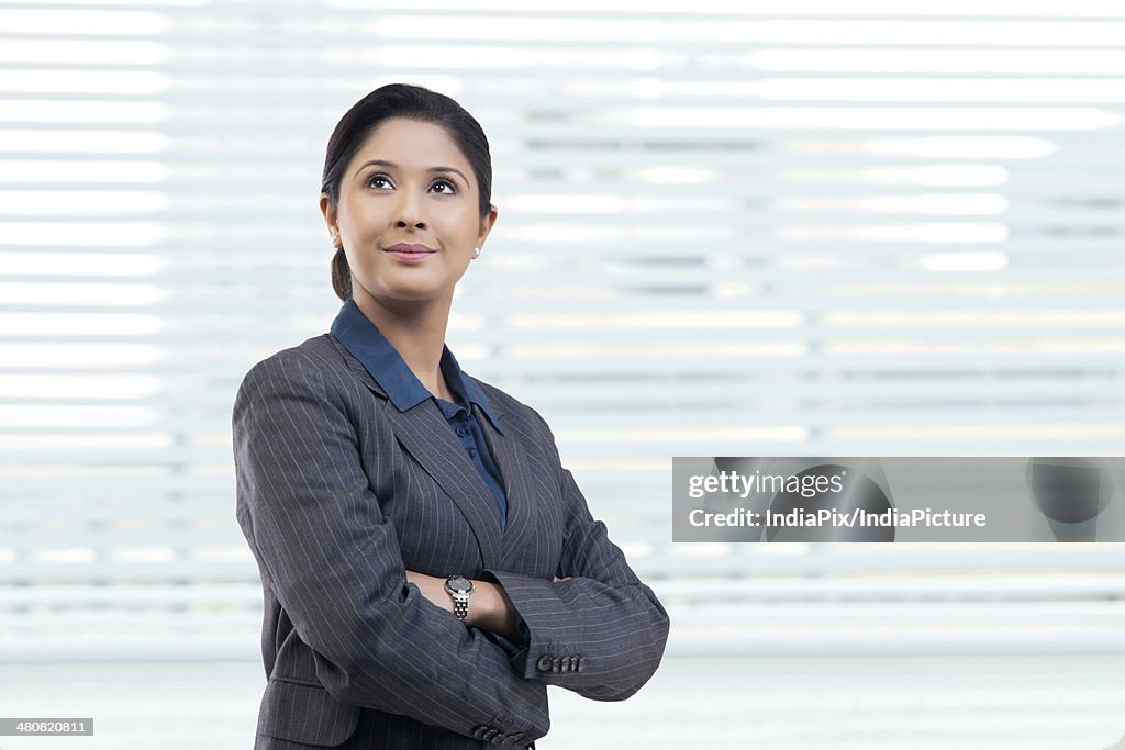 Thoughtful young businesswoman with arms crossed looking away in office