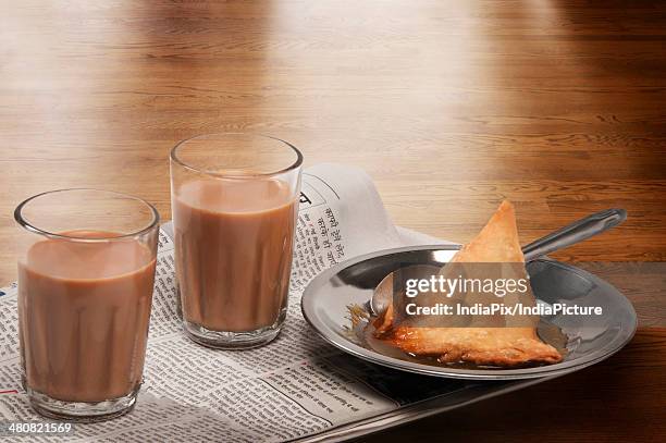 glasses of chai on newspaper with plate of samosa over a wooden surface - samosa stock pictures, royalty-free photos & images