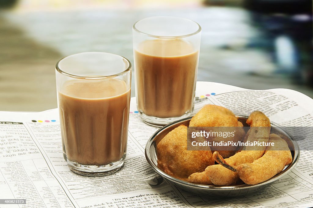 Close-up of morning chai with bhajiyas and vada on newspaper