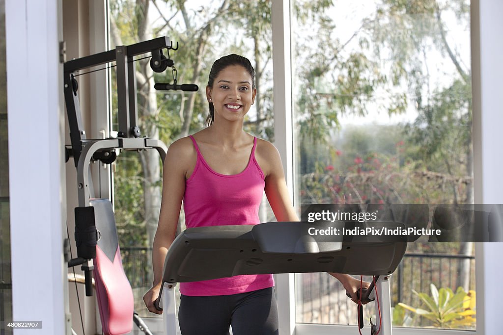 Portrait of happy young woman exercising on treadmill at health club
