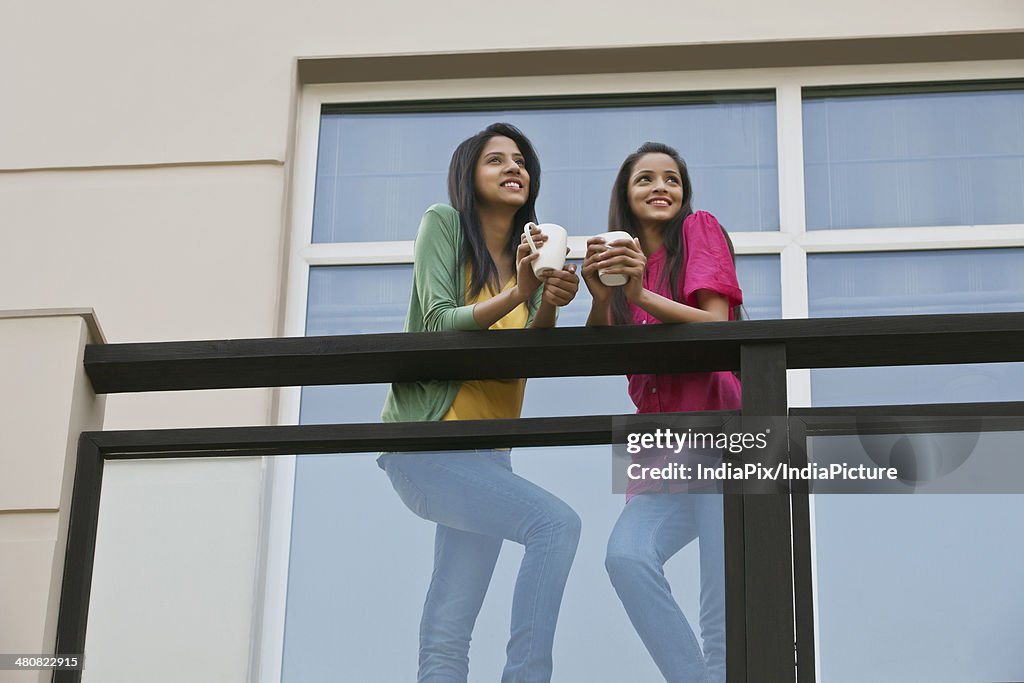 Low angle view of young women looking away while having coffee in balcony