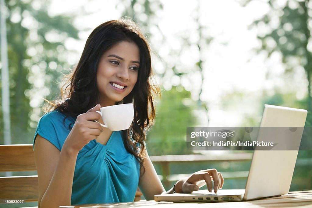 Beautiful young woman having coffee while using laptop at sidewalk cafe