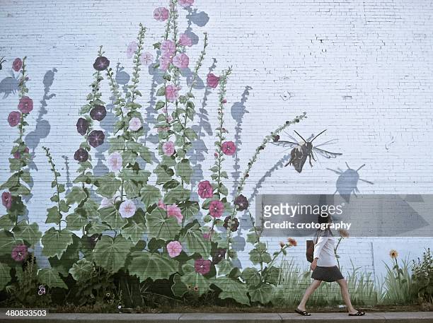 woman walking by flowery wall - muurschildering stockfoto's en -beelden