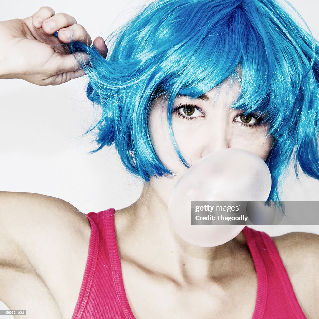 Portrait of a Woman in blue wig blowing bubblegum bubble