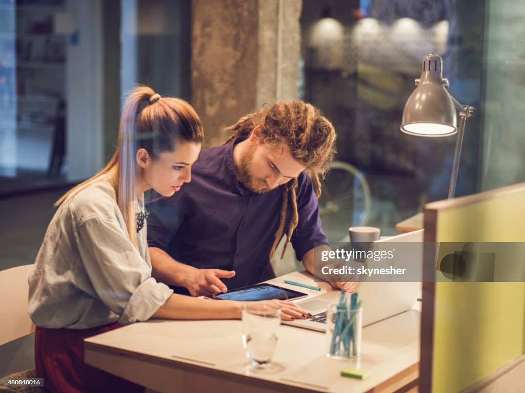 Two young creative people using wireless technology in office.