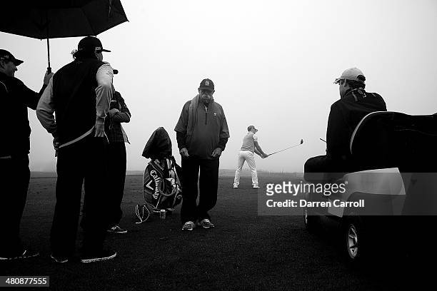 Billy Horschel practices on the range while rules official Colin Murray tells players about a rain delay and caddy Mike "Fluff" Cowan looks on during...