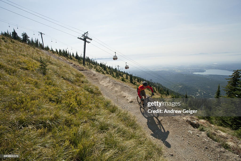 Man mountain biking on trail with ski gondolas.