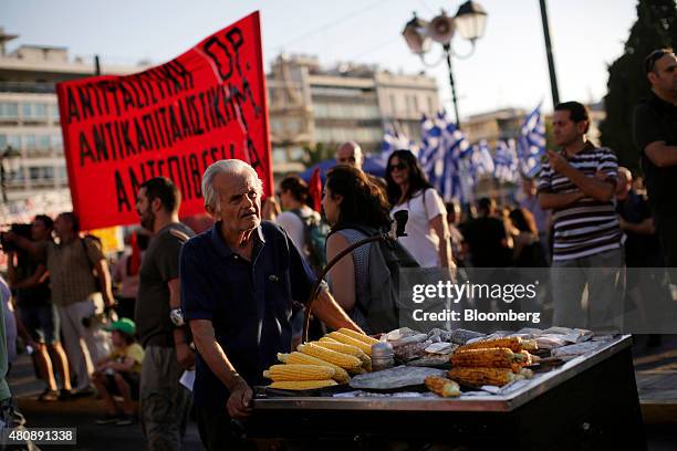 Street vendor selling roasted corn cobs passes anti-bailout protestors on Syntagma Square during a demonstration outside the Greek parliament in...