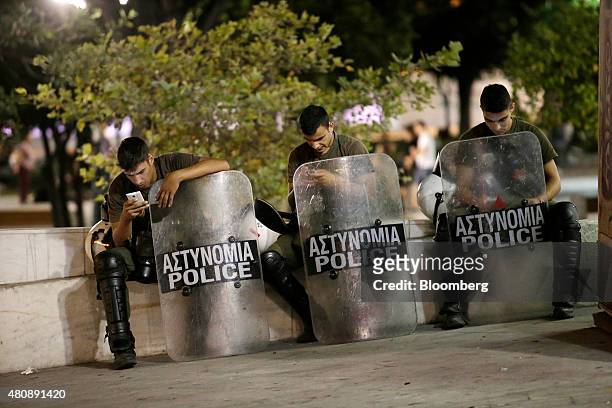 Riot police check their mobile phones while resting following clashes with anti-bailout protestors in central Athens, Greece, on Wednesday, July 15,...