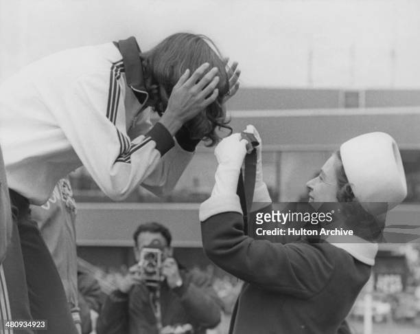 Queen Elizabeth II gets the ribbon entangled in the hair of Debbie Brill of Canada, as she presents her with the gold medal for the High Jump at...