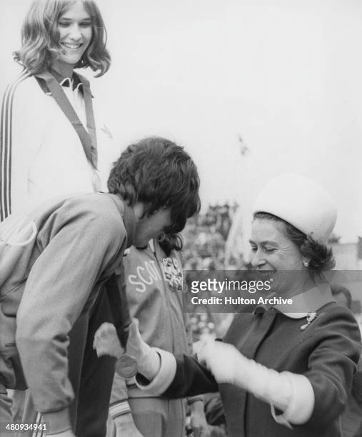 Queen Elizabeth II presents the silver medal for the High Jump to Ann Wilson of England, as gold medalist, Debbie Brill of Canada, looks on, at...