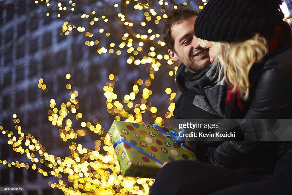 Young couple exchanging gifts next to outdoor xmas lights