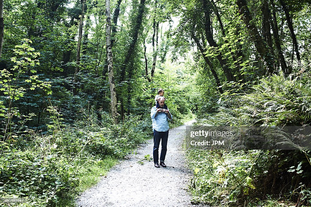 Father carrying baby son on shoulders along country lane