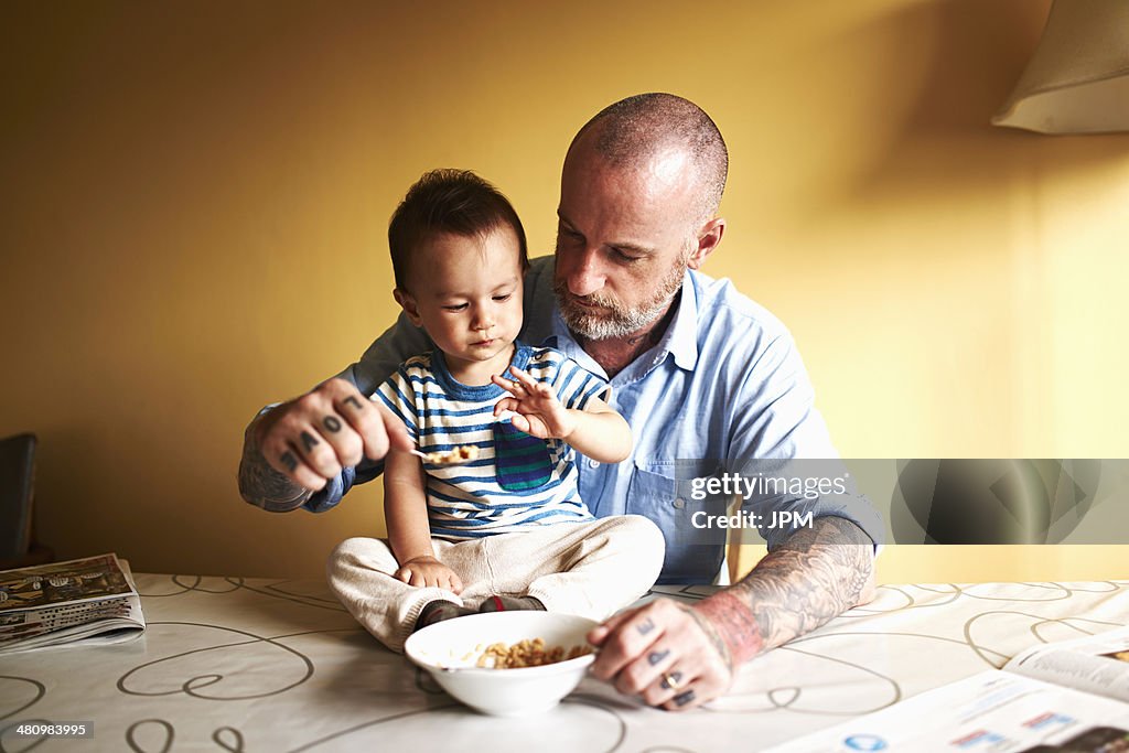 Baby boy sitting on table having cereal with father