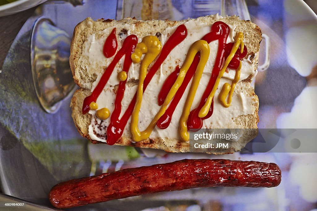 Still life of bread bun, mustard, tomato sauce and a hot dog sausage