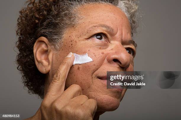 close up studio portrait of senior woman applying face cream - beauty studio moisturisers stock pictures, royalty-free photos & images