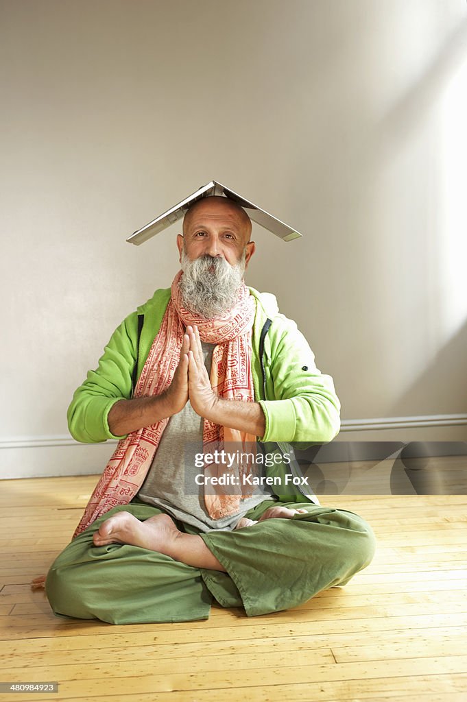 Senior man in lotus position with laptop on head