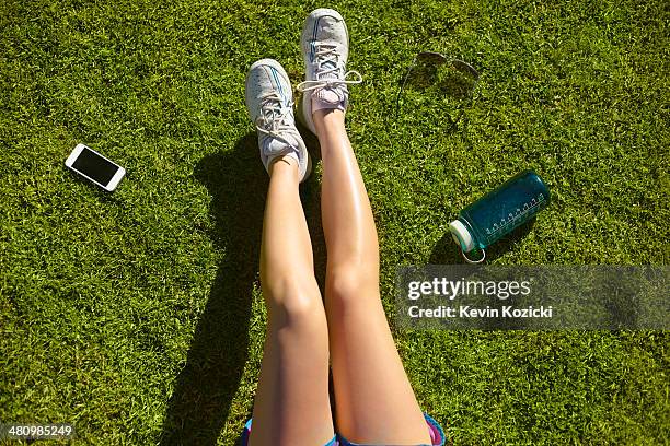 young woman's legs on sunlit grass in park - woman lying down stock pictures, royalty-free photos & images