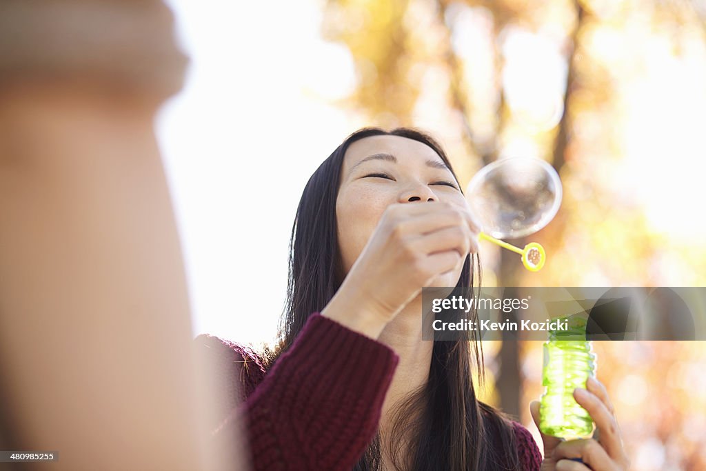 Young woman in park blowing bubbles