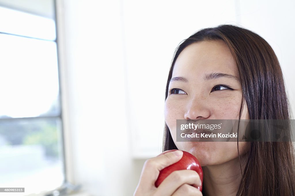 Young woman in kitchen eating red apple