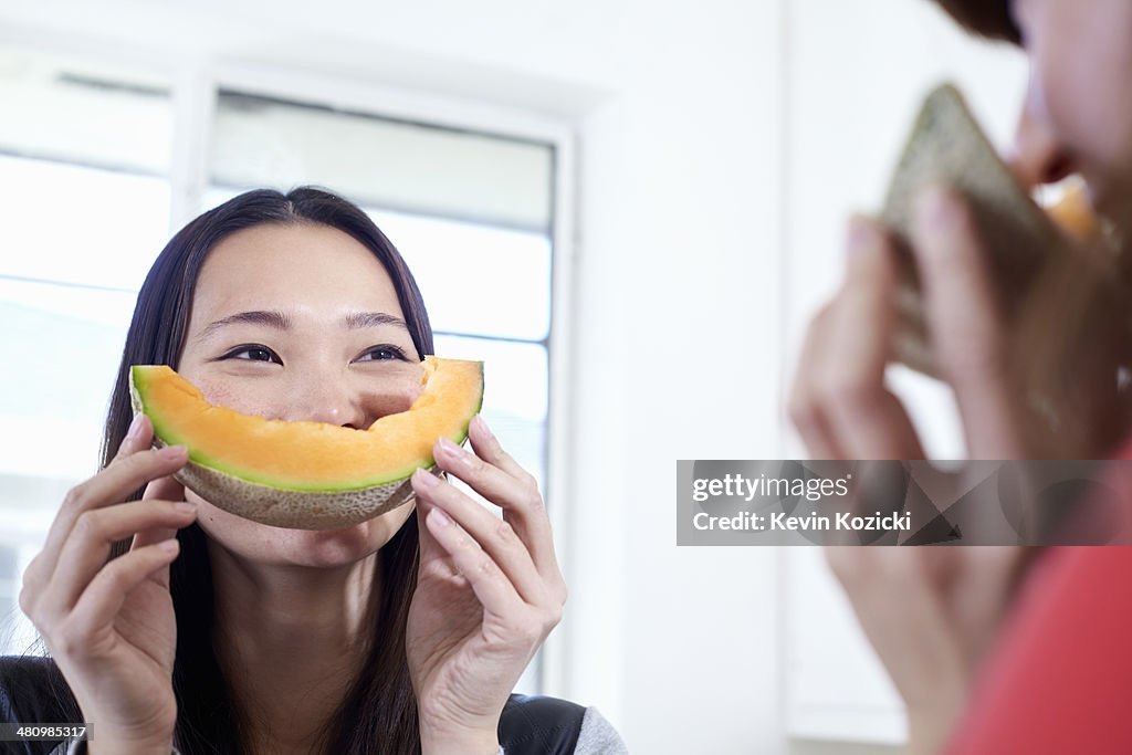 Two young women in kitchen with melon mouths
