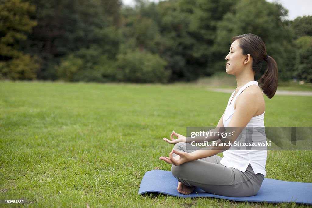 Young woman in park practicing yoga lotus position