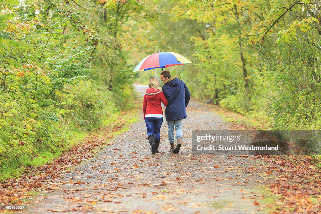 Young couple strolling along country lane with colorful umbrella