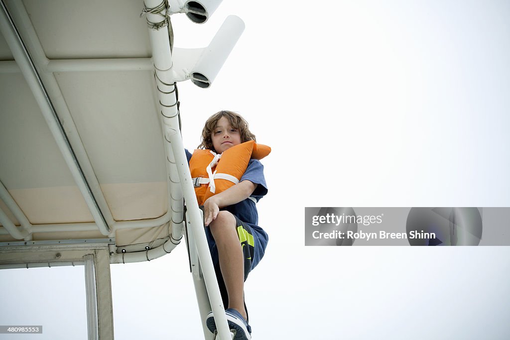 Young boy in life jacket climbing up boat steps