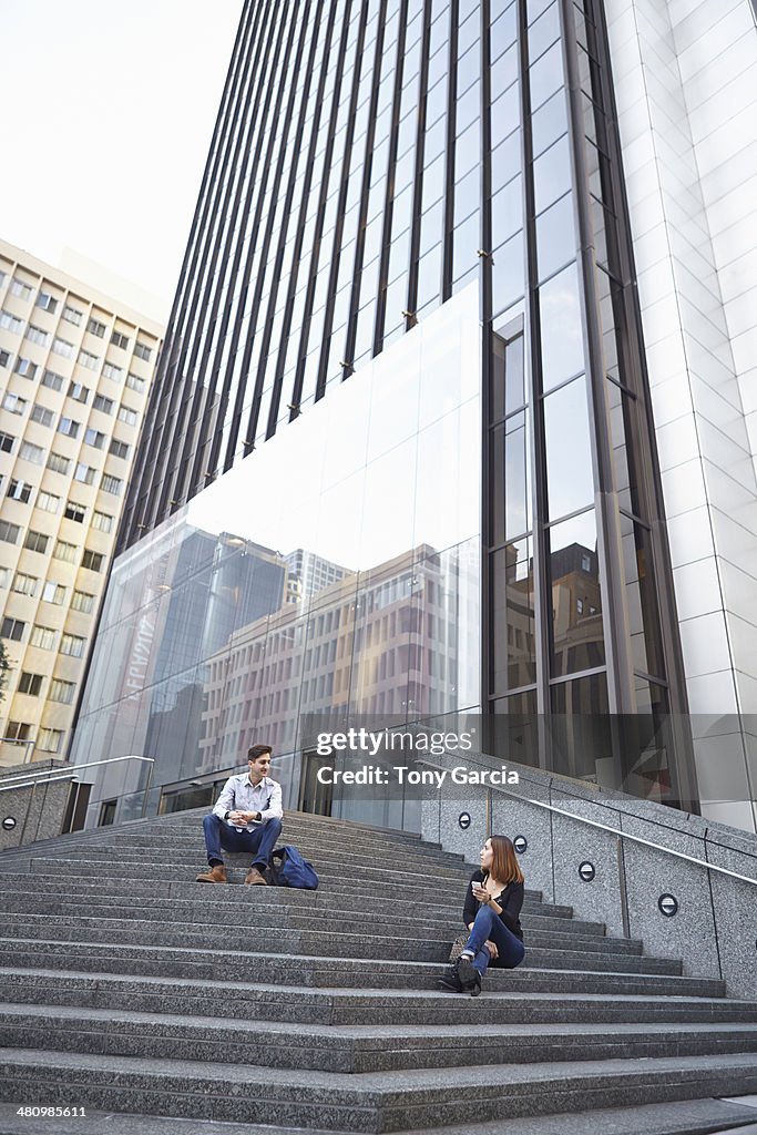 Mid adult man chatting up young woman whilst sitting on steps